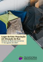 No fundo, barracas de pessoas que moram na rua. Acima, escrito em preto e azul escuro: 